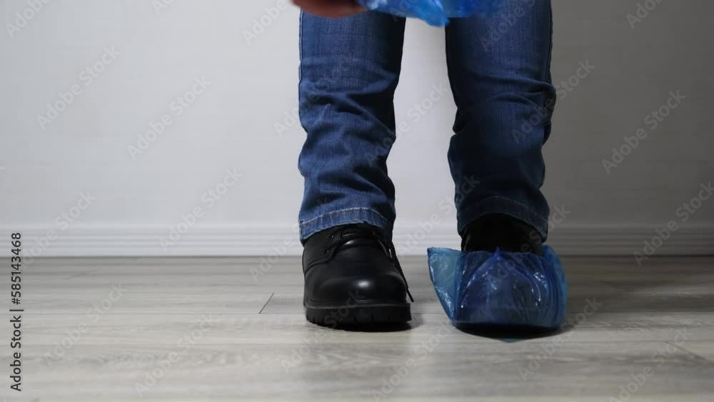 a woman in jeans and black leather boots puts on plastic blue shoe covers while standing on the floor a woman in jeans and black leather boots puts on plastic blue shoe covers while standing on the floor