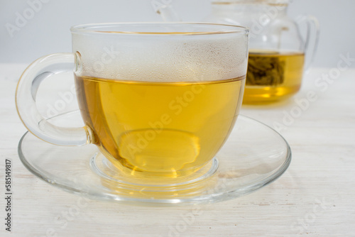 Brewed green tea poured into a glass cup and a teapot on wooden table.