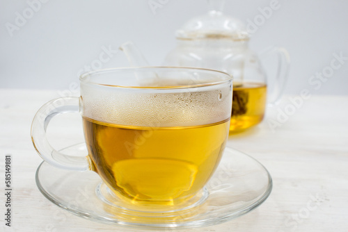 Brewed green tea poured into a glass cup and a teapot on wooden table.