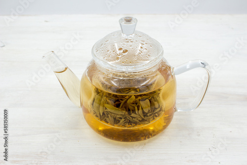 Green tea brewed in a glass teapot on a wooden white table.