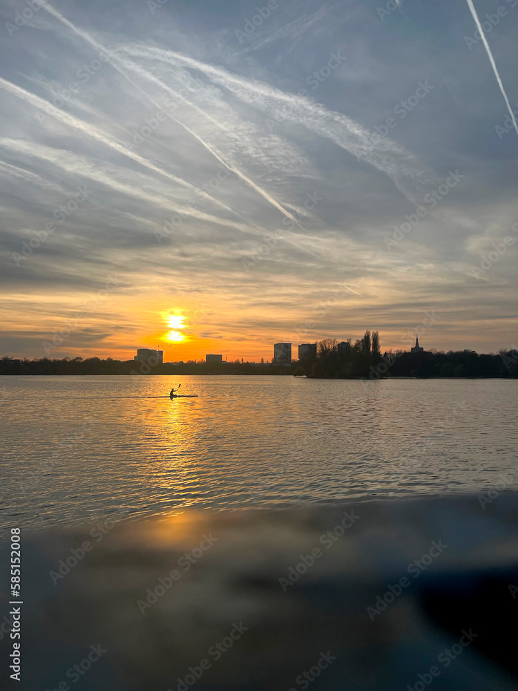 Closeup of sunset on the lake with a canoe on the reflection of the sun and with clouds furrowed by airplane tracks