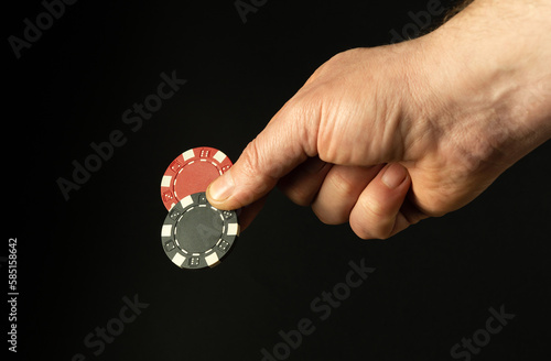 Close-up of a person's hand with two poker chips while betting to win. Free space for advertising on a black background