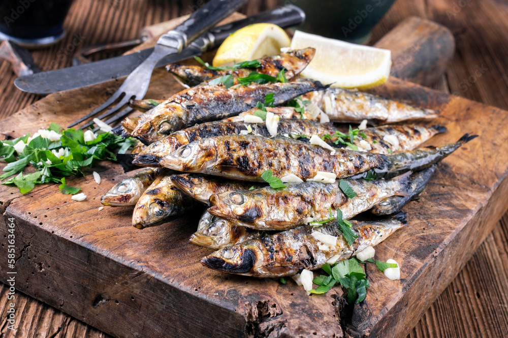 Traditional Italian barbecue anchovies with herb es lemon slices served as close-up on an old rustic wooden board