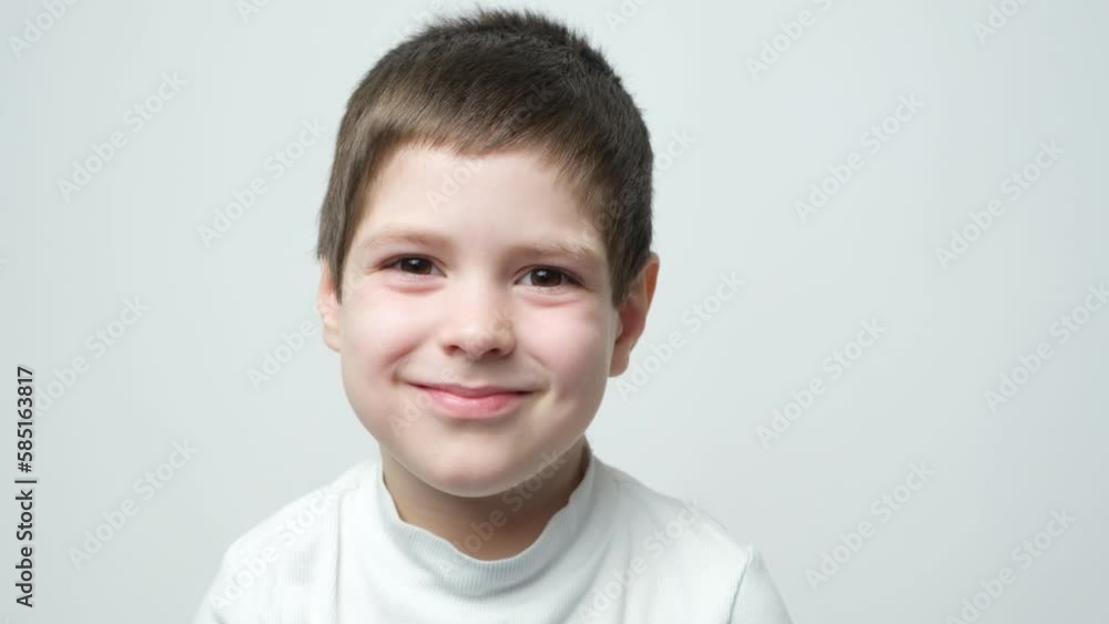 Handsome smart 5 year old brunette boy smiling and staring into the camera, blinking, opening and closing his eyes on a white background Handsome smart 5 year old brunette boy smiling and staring into the camera, blinking, opening and closing his eyes on a white background