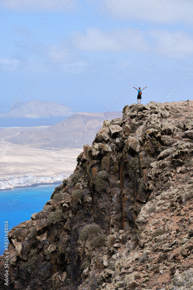 Woman with arms raised on top of a hill. With La Graciosa Island in the background