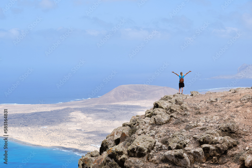 Obraz premium Woman with arms raised on top of a hill. With La Graciosa Island in the background