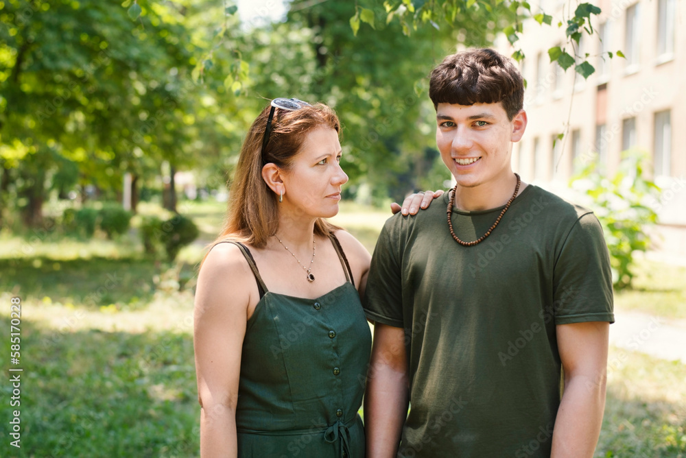A woman looks with pride and joy at her almost adult teenage son, they talk in the park, the boy smiles and tells his mother about his new friends