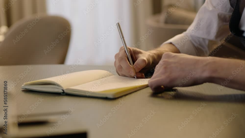 Close-up of male hands and notebook of unidentified young writer. The writer makes notes in a notebook Close-up of male hands and notebook of unidentified young writer. The writer makes notes in a notebook