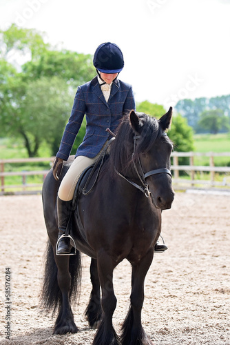 Black Fell pony trotting ridden by girl in saddle and bridle during a dressage test