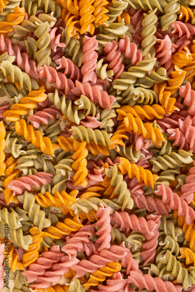 Rice vegetable pasta in the form of spirals, top view. Healthy rice pasta with tomatoes, selenera, carrots and beets
