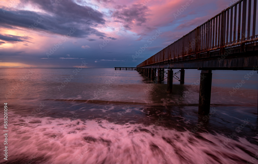 Seascape with dramatic colourful sunset in the ocean. Footpath bridge pier in the sea