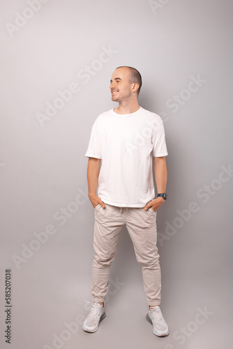 Full body shot of a bald looking aside man standing with hands in pockets.