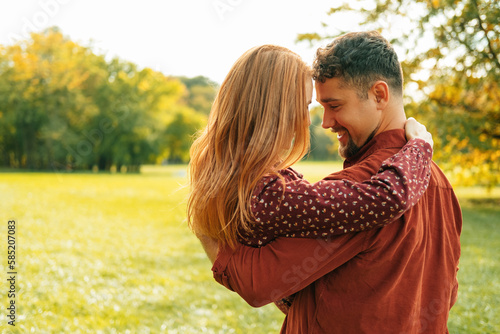 Slika na platnu In love smiling man is holding his red head lover up in arms outdoors