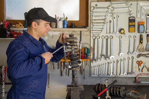 Image of a mechanic in overalls in his workshop while he disassembles a car shock absorber with a wrench and extractors. 
