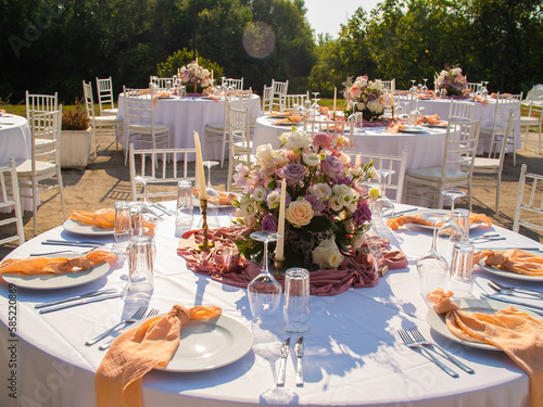Beautiful outdoor wedding decoration in city. Candles and dried flowers and accessories with bouquets and glasses on table with linen tablecloth on newlywed table on green lawn