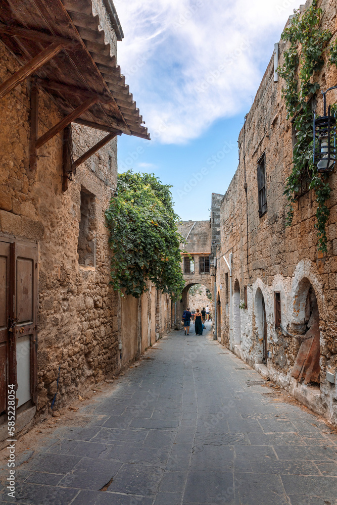 Street view of old town of Rhodes, Greece. Paved roads and pavements with colorful houses and fragrant flowers.
