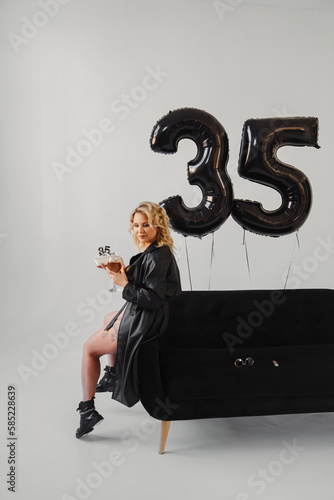 blonde in a black with champagne and cake on the couch. balloons of thirty-five