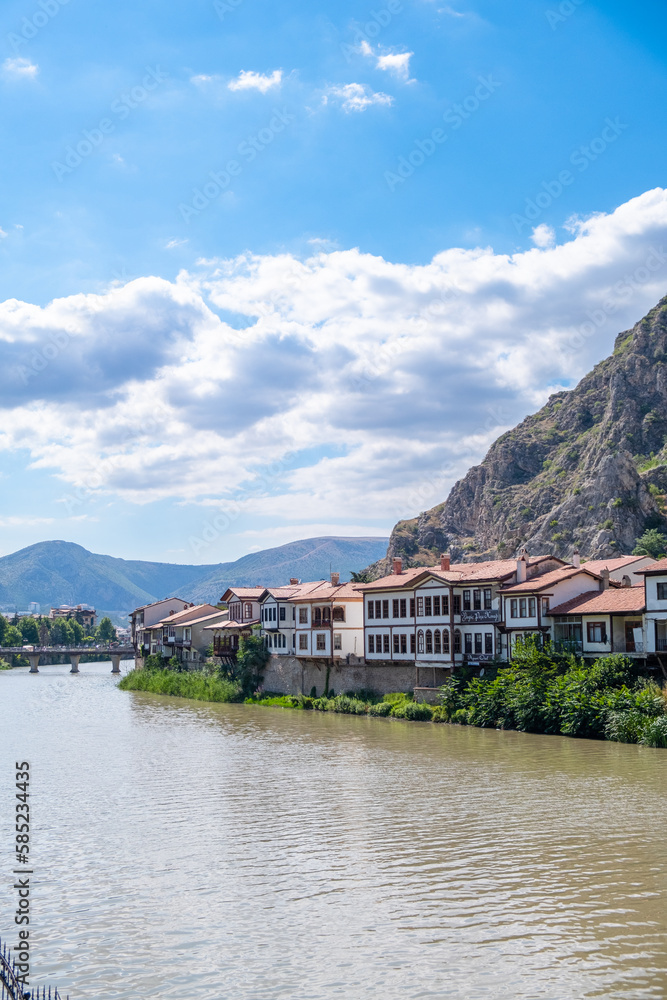 View of old Ottoman houses on the banks of Yesilirmak river in Amasya city. Amasya landscape beautiful river with clouds, sunny summer day. Popular tourist destination in Turkey