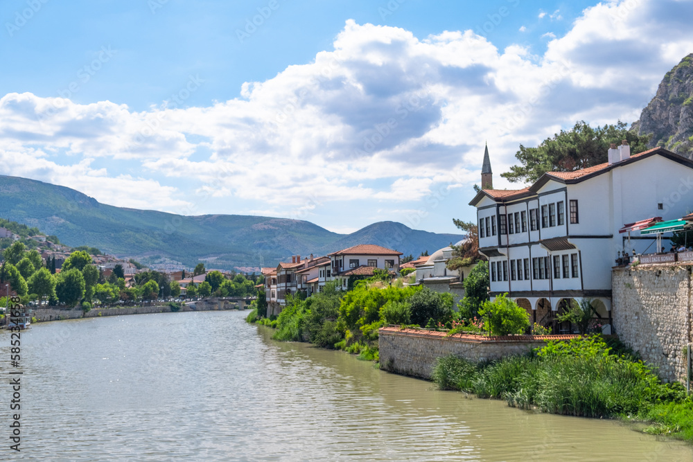 View of old traditional Ottoman houses on the banks of Yesilirmak river in Amasya city. Amasya landscape beautiful river with clouds, sunny summer day. Popular tourist destination in Turkey