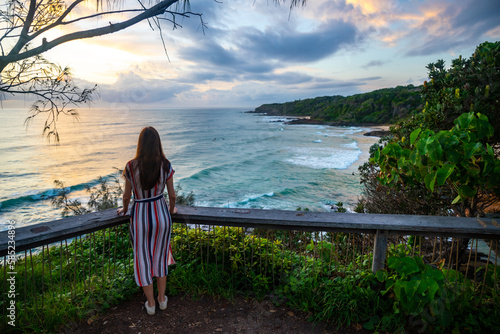 A girl in dress walks along the boardwalk and enjoys the view of the stunning first and second bay Coolum and big waves on Pacific Ocean. Stunning panorama of Sunshine Coast, Queensland, Australia photo