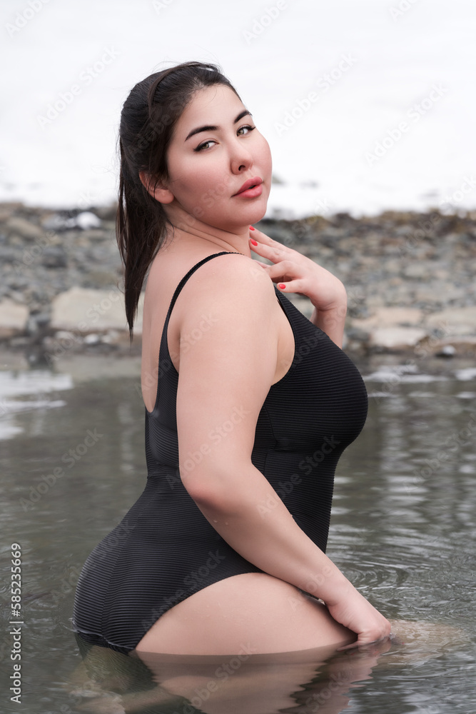 Busty curvy extended sizes young adult model in black one-piece bathing  suit sitting in outdoors