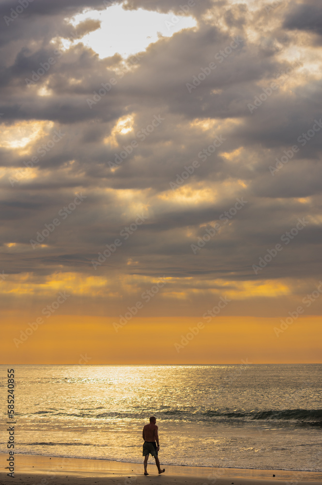 Silhouette of a lonely man walking along the coast heading towards the sea with the sunset in the background in a sea that reflects the sunlight