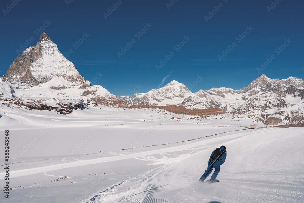 Young man skiing in Zermatt ski resort right next to the famous Matterhorn peak. Beautiful sunny day for snowboarding. Winter sports concept.