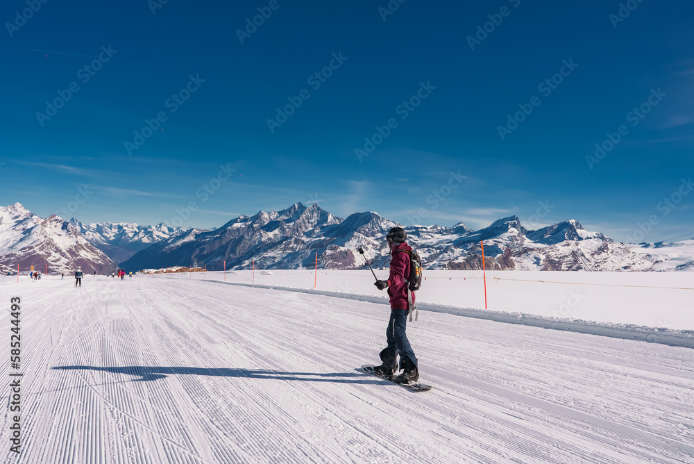 Young man snowboarding in Zermatt ski resort right next to the famous Matterhorn peak. Beautiful sunny day for snowboarding. Winter sports concept.