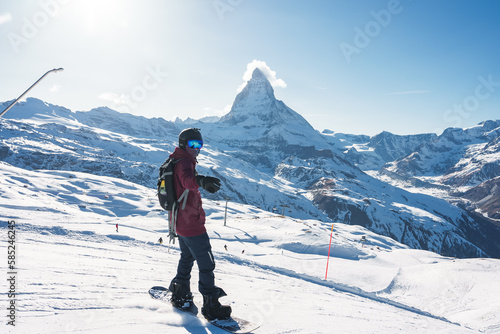 Young man snowboarding in Zermatt ski resort right next to the famous Matterhorn peak. Beautiful sunny day for snowboarding. Winter sports concept.