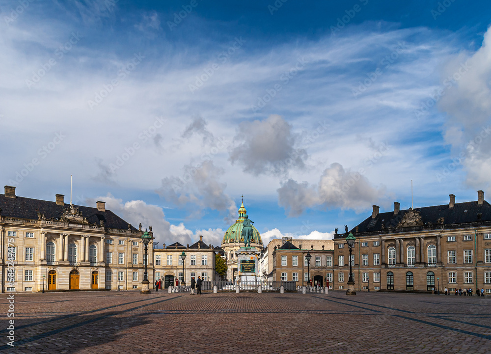 Copenhagen, Denmark - September 13, 2010: wide view of Amalienborg circle with royal palaces and green dome of Frederiks church in back behind equestrian statue of king Frederik V. Blue cloudscape