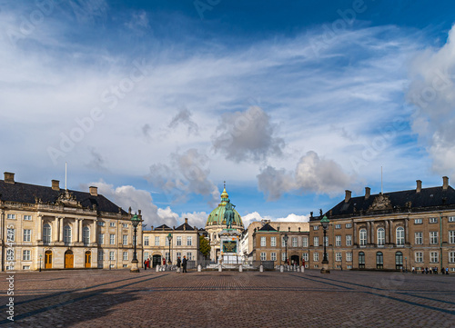 Copenhagen, Denmark - September 13, 2010: wide view of Amalienborg circle with royal palaces and green dome of Frederiks church in back behind equestrian statue of king Frederik V. Blue cloudscape