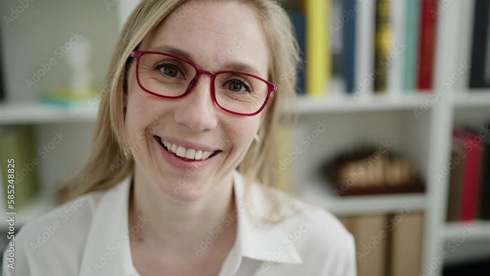 Young blonde woman teacher smiling confident sitting on table at library university Young blonde woman teacher smiling confident sitting on table at library university