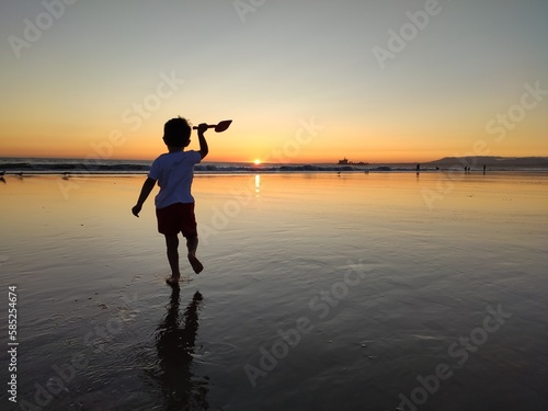 Criança a brincar na praia com por do sol