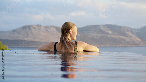 Silhouette of young unrecognizable woman at midday in infinity pool on edge of abyss. girl looks into distance  concept of loneliness and happiness to be alone for peace and tranquility.
