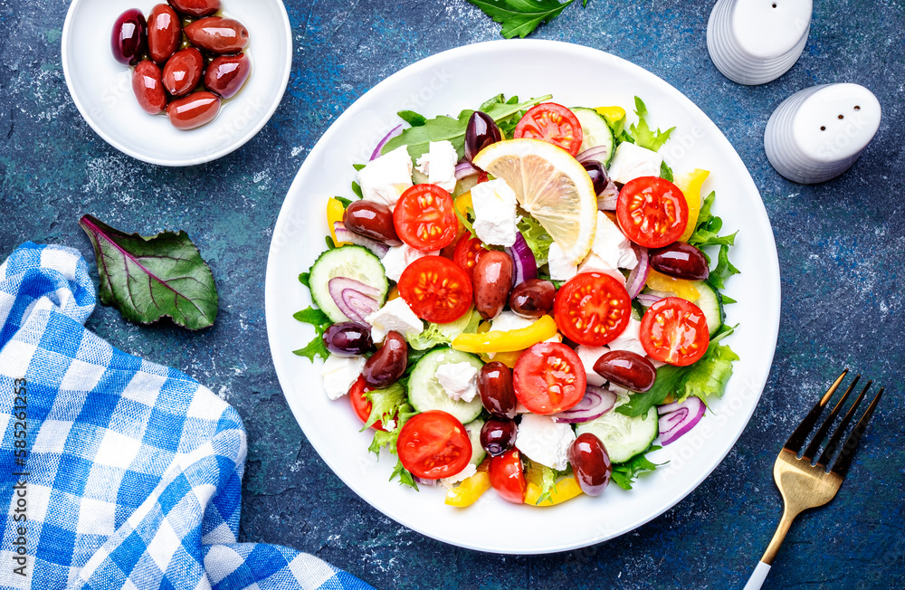 Greek salad with feta cheese, kalamata olives, red tomato, yellow paprika, cucumber and onion, healthy mediterranean diet food, low calories eating. Blue stone background, top view Greek salad with feta cheese, kalamata olives, red tomato, yellow paprika, cucumber and onion, healthy mediterranean diet food, low calories eating. Blue stone background, top view