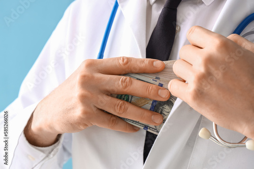Male doctor hiding bribe on blue background, closeup
