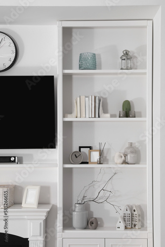 Stylish shelves with different decor elements and TV set in room. Interior design