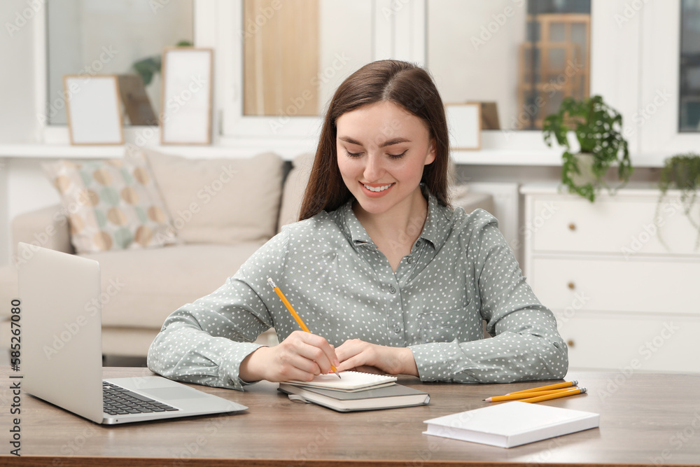 Happy young woman writing in notebook at wooden table indoors Happy young woman writing in notebook at wooden table indoors