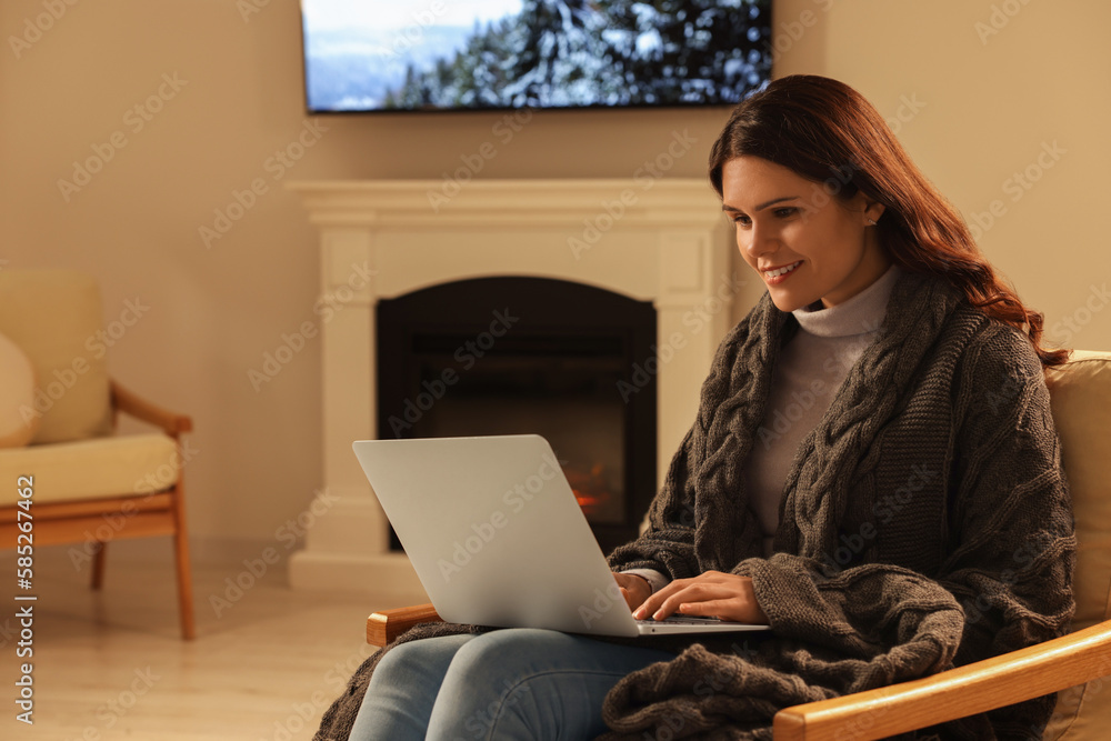 Fototapeta premium Young woman working on laptop near fireplace at home