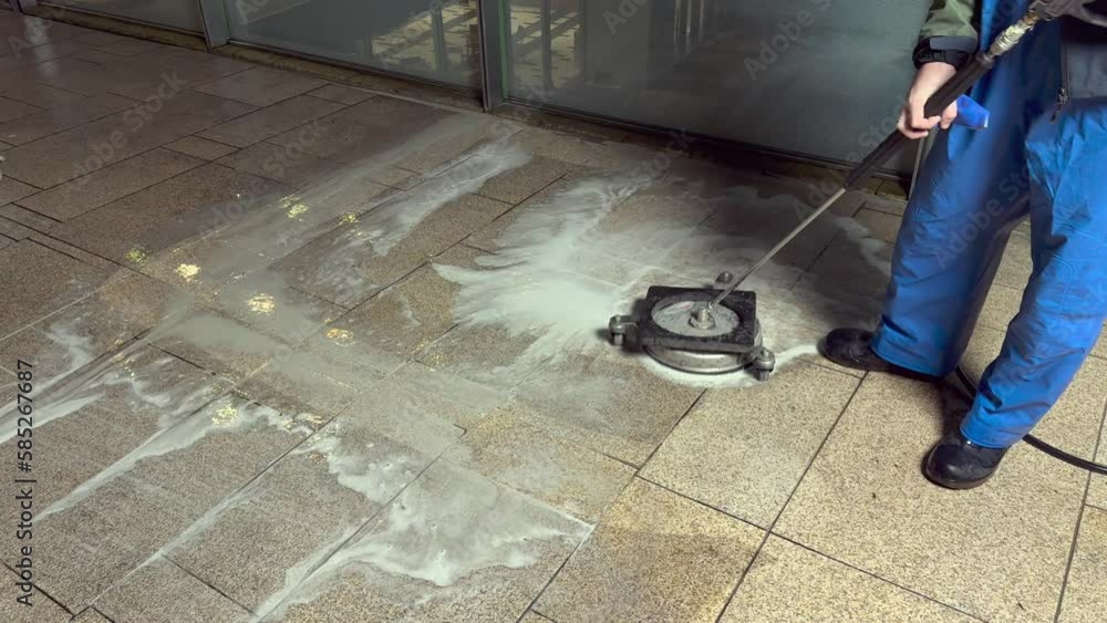 A workman cleans a dirty beige granite floor with a high pressure cleaner A workman cleans a dirty beige granite floor with a high pressure cleaner