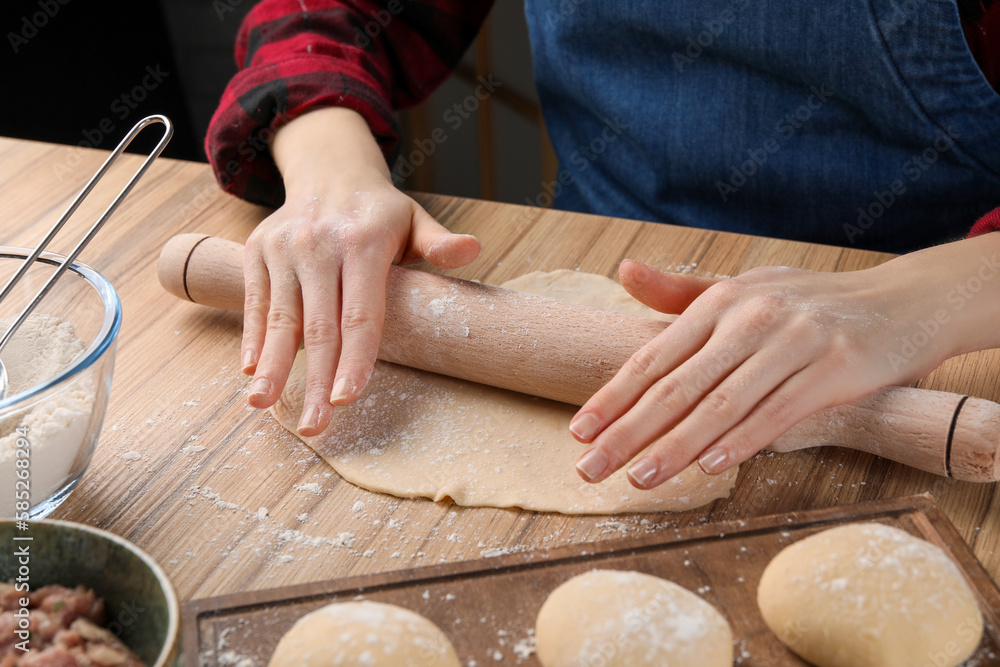 Woman rolling dough for chebureki at wooden table, closeup