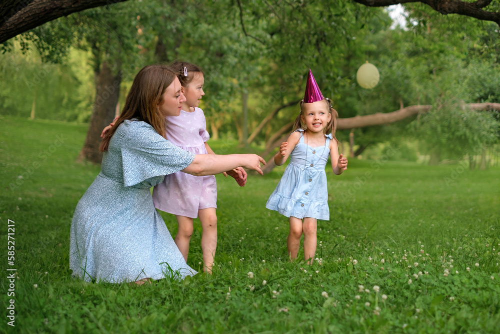 Fototapeta premium Funny naughty girl tells congratulations to friend on birthday and sings a song. A family celebrates a holiday in the park on a warm summer day.