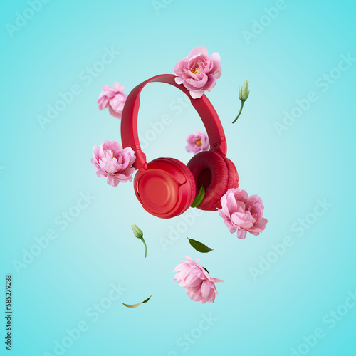Red headphones and flowers levitating on blue background. Music, flowers, spring background. Creative spring or music minimal arrangement