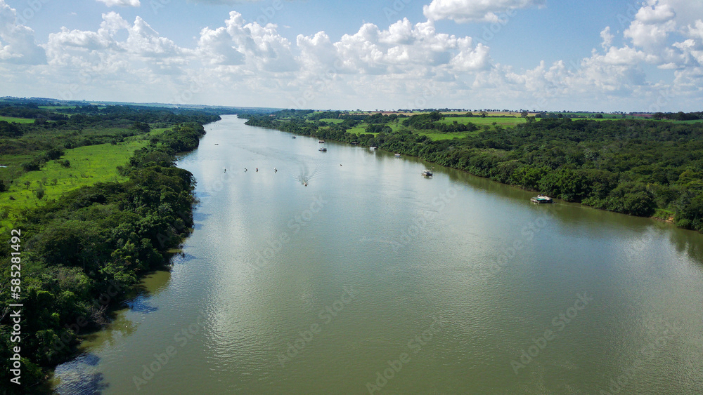 Fototapeta premium Aerial view of the Rio Grande river with lush forested banks, under a blue sky, in Orindiuva/SP, on the border of São Paulo and Minas Gerais, Brazil