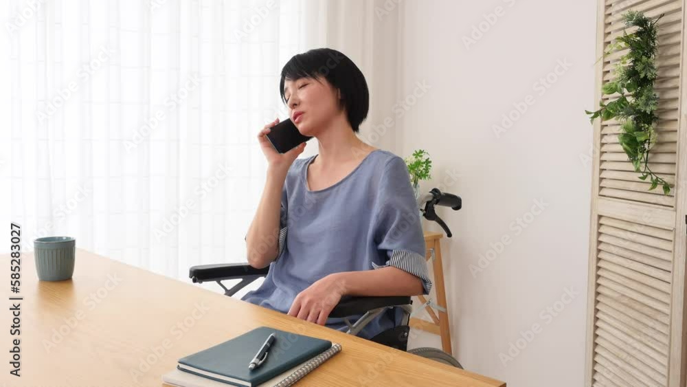 リビングでスマートフォンで電話する車椅子に乗った女性 リビングでスマートフォンで電話する車椅子に乗った女性