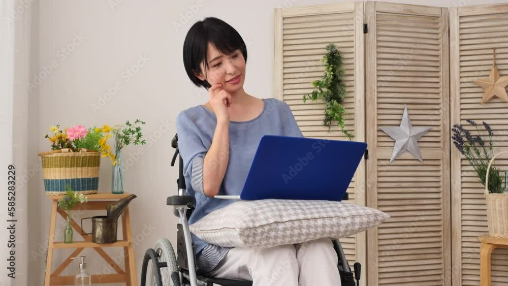 リビングでノートパソコンを見る車椅子に乗った女性 リビングでノートパソコンを見る車椅子に乗った女性