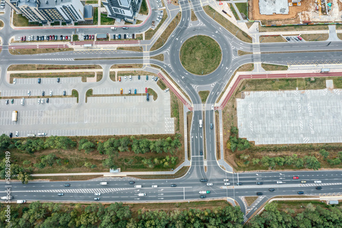 road junction with roundabout and parking lot with parked cars. top down aerial view