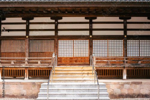 Frontal view of a Japanese temple with wooden beams and a staircase in the middle. The facade impresses with the traditional square paper windows.