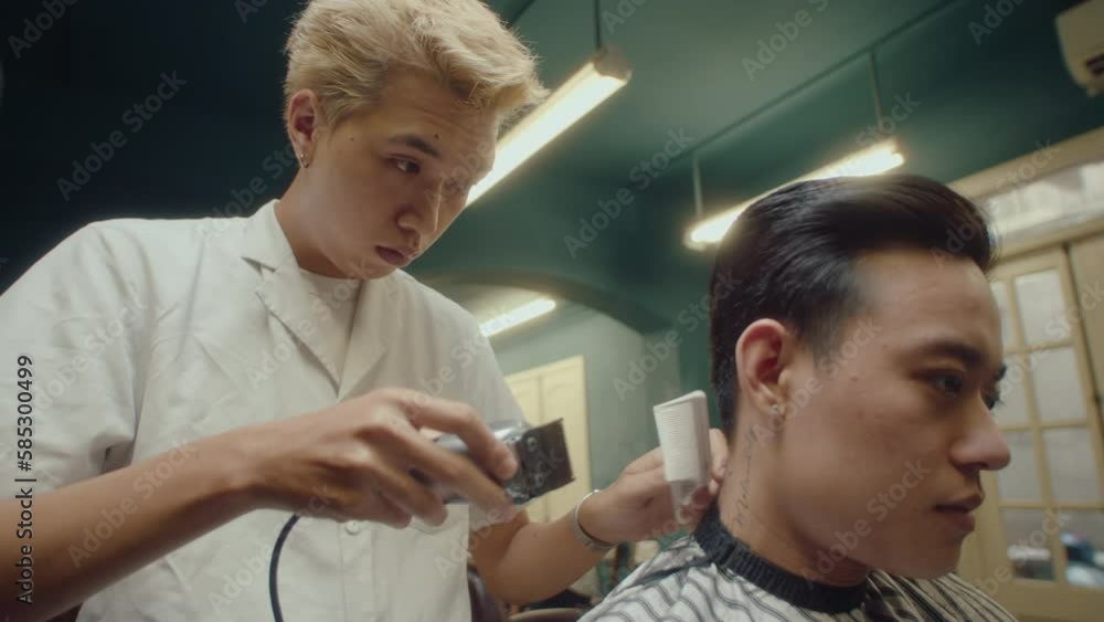 Young Asian barber lining up the back of the head using hair clippers and comb, giving a haircut