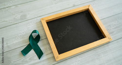 A dark green ribbon and a small black board, Concept related to medical awareness Selective focus photo